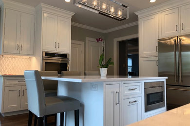 Mid-sized transitional u-shaped separate kitchen in New York with an undermount sink, beaded inset cabinets, white cabinets, quartz benchtops, white splashback, ceramic splashback, stainless steel appliances, dark hardwood floors, with island, brown floor and white benchtop.