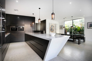 This is an example of a contemporary u-shaped eat-in kitchen in Melbourne with an integrated sink, flat-panel cabinets, dark wood cabinets, limestone benchtops, stainless steel appliances, concrete floors, with island, grey floor and white benchtop.