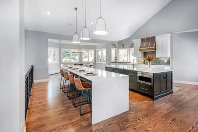 Photo of an expansive contemporary eat-in kitchen in Denver with an undermount sink, raised-panel cabinets, white cabinets, quartzite benchtops, green splashback, stainless steel appliances, dark hardwood floors, multiple islands, brown floor, white benchtop and vaulted.
