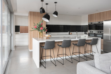 This is an example of a scandinavian l-shaped open plan kitchen in Perth with an undermount sink, flat-panel cabinets, white cabinets, black splashback, glass sheet splashback, stainless steel appliances, with island, grey floor and white benchtop.