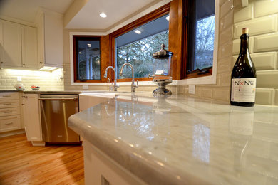Eat-in kitchen - transitional u-shaped eat-in kitchen idea in Portland with a farmhouse sink, white cabinets, white backsplash, stainless steel appliances, shaker cabinets, quartzite countertops and porcelain backsplash