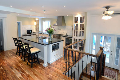 Example of a mid-sized transitional l-shaped medium tone wood floor eat-in kitchen design in Toronto with a double-bowl sink, raised-panel cabinets, white cabinets, solid surface countertops, black backsplash, stone slab backsplash, stainless steel appliances and an island