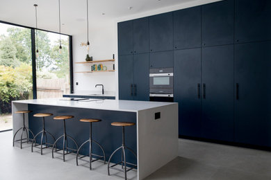 This is an example of an expansive modern galley open plan kitchen in London with an integrated sink, flat-panel cabinets, blue cabinets, quartzite benchtops, cement tiles, with island, grey floor and white benchtop.