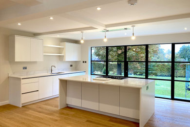 Large contemporary open plan kitchen in Surrey with a double-bowl sink, flat-panel cabinets, white cabinets, quartz worktops, white splashback, marble splashback, black appliances, light hardwood flooring, an island, white worktops, exposed beams and feature lighting.