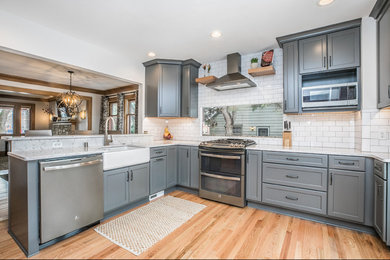 Design ideas for a traditional kitchen in Milwaukee with a farmhouse sink, recessed-panel cabinets, grey cabinets, quartzite benchtops, white splashback, porcelain splashback and light hardwood floors.