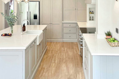 This is an example of a traditional l-shaped open plan kitchen in Other with a belfast sink, shaker cabinets, grey cabinets, quartz worktops, white splashback, stone slab splashback, stainless steel appliances, an island, white worktops and a chimney breast.