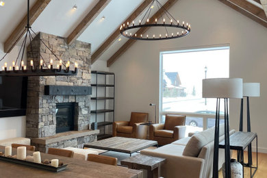 Example of a mountain style open concept laminate floor, orange floor and exposed beam living room design in Other with white walls and a stone fireplace