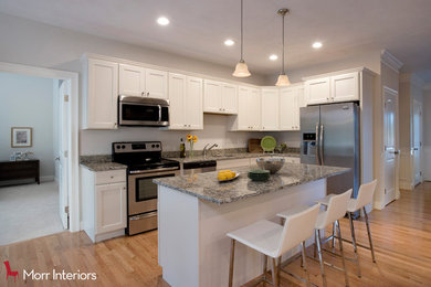 Example of a trendy l-shaped brown floor kitchen design in Boston with an undermount sink, white cabinets, stainless steel appliances and an island