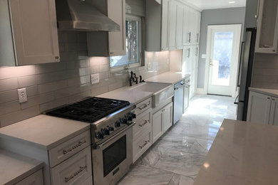 Mid-sized minimalist porcelain tile and white floor kitchen pantry photo in Other with a farmhouse sink, shaker cabinets, white cabinets, granite countertops, gray backsplash, ceramic backsplash, stainless steel appliances, an island and white countertops