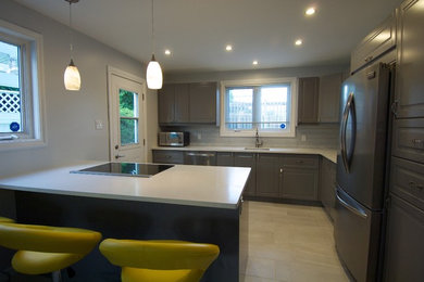 Mid-sized trendy l-shaped porcelain tile and gray floor eat-in kitchen photo in Ottawa with a single-bowl sink, raised-panel cabinets, gray cabinets, quartz countertops, gray backsplash, glass sheet backsplash, stainless steel appliances and a peninsula