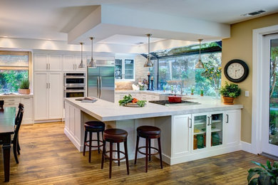 Large trendy l-shaped medium tone wood floor eat-in kitchen photo in Sacramento with an undermount sink, recessed-panel cabinets, white cabinets, marble countertops, beige backsplash, cement tile backsplash, stainless steel appliances and a peninsula