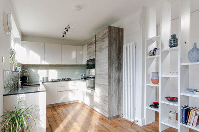 Mid-sized modern open plan kitchen in London with quartzite benchtops, green splashback, porcelain splashback and panelled appliances.