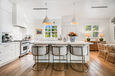 Example of a transitional l-shaped medium tone wood floor, brown floor and shiplap ceiling eat-in kitchen design in Miami with shaker cabinets, white cabinets, white backsplash, stone slab backsplash, stainless steel appliances, an island and white countertops