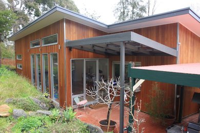 Photo of a mid-sized contemporary one-storey black house exterior in Adelaide with wood siding, a flat roof and a metal roof.