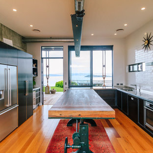 Large eclectic kitchen pantry appliance - Inspiration for a large eclectic galley medium tone wood floor kitchen pantry remodel in Wellington with an undermount sink, black cabinets, stainless steel countertops, white backsplash, cement tile backsplash, stainless steel appliances and an island