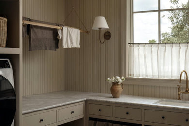 Transitional l-shaped wallpaper laundry room photo in Austin with an undermount sink, flat-panel cabinets, beige cabinets, a side-by-side washer/dryer and gray countertops