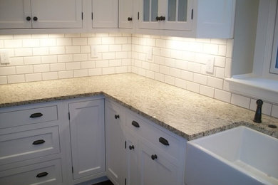 Example of a mid-sized classic l-shaped dark wood floor and brown floor enclosed kitchen design in Boston with a farmhouse sink, shaker cabinets, white cabinets, granite countertops, white backsplash, subway tile backsplash, stainless steel appliances and multicolored countertops