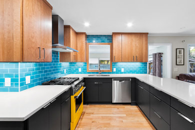 Example of an eclectic light wood floor and brown floor kitchen design in Other with flat-panel cabinets, brown cabinets, blue backsplash, subway tile backsplash, stainless steel appliances and white countertops