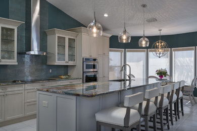 Mid-sized beach style l-shaped eat-in kitchen photo in Tampa with an undermount sink, recessed-panel cabinets, white cabinets, blue backsplash, glass tile backsplash, stainless steel appliances and an island