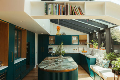 Photo of a contemporary u-shaped kitchen in London with a double-bowl sink, shaker cabinets, turquoise cabinets, white splashback, stone slab splashback, black appliances, medium hardwood flooring, an island, brown floors and white worktops.