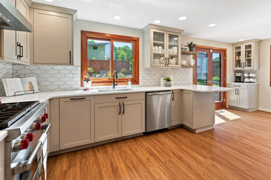 Foto på ett avskilt, mellanstort amerikanskt vit u-kök, med en undermonterad diskho, skåp i shakerstil, beige skåp, bänkskiva i kvarts, vitt stänkskydd, stänkskydd i keramik, rostfria vitvaror, mellanmörkt trägolv, en halv köksö och flerfärgat golv