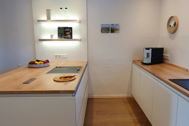 Offene, Zweizeilige, Mittelgroße Klassische Küche mit integriertem Waschbecken, flächenbündigen Schrankfronten, weißen Schränken, Arbeitsplatte aus Holz, Küchenrückwand in Weiß, Rückwand-Fenster, Elektrogeräten mit Frontblende, dunklem Holzboden, Halbinsel, braunem Boden und brauner Arbeitsplatte in Düsseldorf