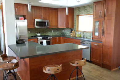 This is an example of a mid-sized transitional l-shaped eat-in kitchen in Sacramento with an undermount sink, shaker cabinets, medium wood cabinets, granite benchtops, green splashback, subway tile splashback, stainless steel appliances, light hardwood floors, with island and brown floor.