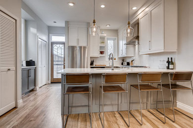 Design ideas for a small transitional u-shaped eat-in kitchen in Denver with an undermount sink, shaker cabinets, white cabinets, granite benchtops, white splashback, ceramic splashback, stainless steel appliances, light hardwood floors, a peninsula, brown floor and white benchtop.