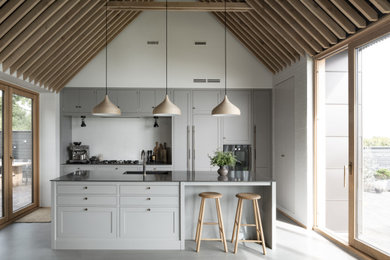 Inspiration for a mid-sized traditional single-wall open plan kitchen in Copenhagen with a single-bowl sink, raised-panel cabinets, grey cabinets, quartzite benchtops, black appliances, concrete floors, with island, grey floor, black benchtop and exposed beam.
