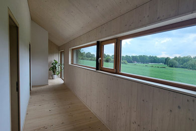 Großer Moderner Flur mit beiger Wandfarbe, hellem Holzboden, freigelegten Dachbalken und Holzwänden in München