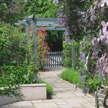 Sandstone paved path leading under a painted pergola