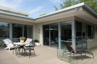 Photo of a large beach style backyard and ground level deck in Melbourne with no cover and glass railing.