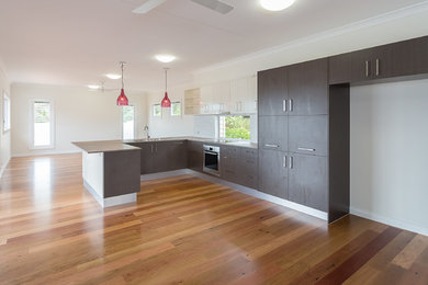 This is an example of a modern u-shaped eat-in kitchen in Brisbane with an undermount sink, dark wood cabinets, quartz benchtops, white splashback, glass tile splashback, stainless steel appliances, light hardwood floors and multiple islands.