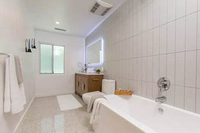 This is an example of a large modern wet room bathroom in Los Angeles with flat-panel cabinets, dark wood cabinets, a freestanding tub, gray tile, porcelain tile, white walls, concrete floors, grey floor, an open shower and a two-piece toilet.