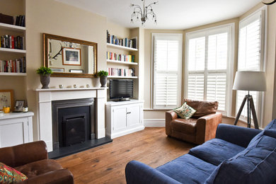 Photo of a mid-sized modern formal enclosed living room in London with beige walls, a standard fireplace, a freestanding tv, a stone fireplace surround and medium hardwood floors.