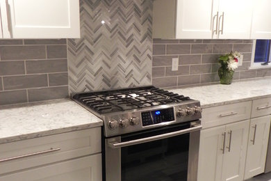 Example of a mid-sized transitional l-shaped ceramic tile enclosed kitchen design in Boston with an undermount sink, recessed-panel cabinets, white cabinets, quartz countertops, gray backsplash, ceramic backsplash, stainless steel appliances and an island
