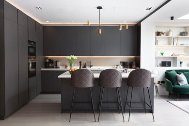 Inspiration for a large modern grey and black l-shaped open plan kitchen in London with a built-in sink, flat-panel cabinets, grey cabinets, engineered stone countertops, yellow splashback, ceramic splashback, black appliances, light hardwood flooring, an island, grey floors, white worktops, a drop ceiling and feature lighting.
