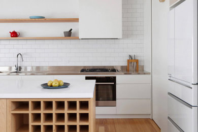 Design ideas for a medium sized contemporary galley open plan kitchen in Melbourne with a built-in sink, shaker cabinets, light wood cabinets, composite countertops, white splashback, metro tiled splashback, white appliances, light hardwood flooring, an island and white worktops.