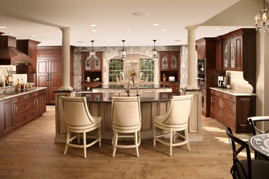 Inspiration for a large rustic open concept kitchen remodel in New York with a farmhouse sink, raised-panel cabinets, brown cabinets, granite countertops, beige backsplash, paneled appliances and two islands