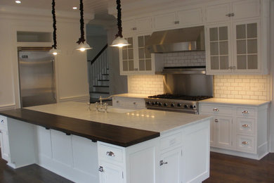 Example of a huge classic u-shaped dark wood floor eat-in kitchen design in New York with a farmhouse sink, beaded inset cabinets, white cabinets, marble countertops, white backsplash, subway tile backsplash, stainless steel appliances and an island