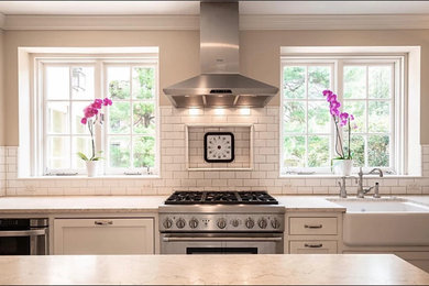 Elegant eat-in kitchen photo in Philadelphia with a farmhouse sink, white backsplash, stainless steel appliances, an island and beige countertops