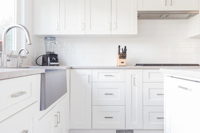 Large transitional l-shaped kitchen in Vancouver with a farmhouse sink, shaker cabinets, white cabinets, white splashback, subway tile splashback, dark hardwood floors and with island.