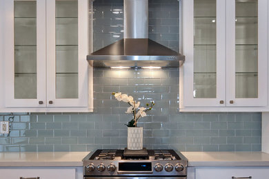 Eat-in kitchen - mid-sized transitional l-shaped medium tone wood floor eat-in kitchen idea in Orange County with a farmhouse sink, shaker cabinets, white cabinets, quartz countertops, gray backsplash, glass tile backsplash, stainless steel appliances and a peninsula