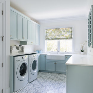 シカゴのビーチスタイルのおしゃれな洗濯室 (エプロンフロントシンク、シェーカースタイル扉のキャビネット、青いキャビネット、白い壁、左右配置の洗濯機・乾燥機、マルチカラーの床、白いキッチンカウンター) の写真