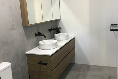 Inspiration for a mid-sized industrial 3/4 bathroom in Brisbane with furniture-like cabinets, medium wood cabinets, a curbless shower, gray tile, ceramic tile, white walls, cement tiles, a vessel sink, engineered quartz benchtops, grey floor, an open shower and white benchtops.