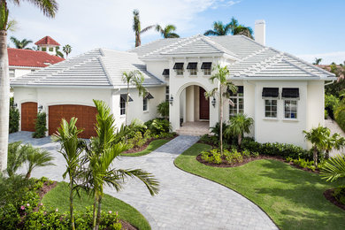 Large tropical two-storey stucco beige house exterior in Miami with a hip roof and a shingle roof.
