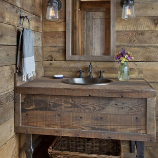 Mountain style brown floor and medium tone wood floor bathroom photo in Other with furniture-like cabinets, dark wood cabinets, brown walls, a drop-in sink, wood countertops and brown countertops