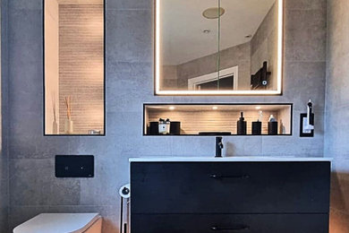 Inspiration for a medium sized bathroom in Surrey with flat-panel cabinets, black cabinets, a built-in bath, a walk-in shower, a wall mounted toilet, grey tiles, grey walls, brown floors, white worktops, a wall niche, a single sink and a floating vanity unit.