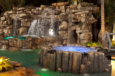 Design ideas for a large country backyard custom-shaped lap pool in Miami with natural stone pavers and a hot tub.