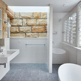 This is an example of a beach style master bathroom in Sydney with white tile, open cabinets, white cabinets, a freestanding tub, an alcove shower, multi-coloured walls, concrete floors, a wall-mount sink, grey floor and a hinged shower door.